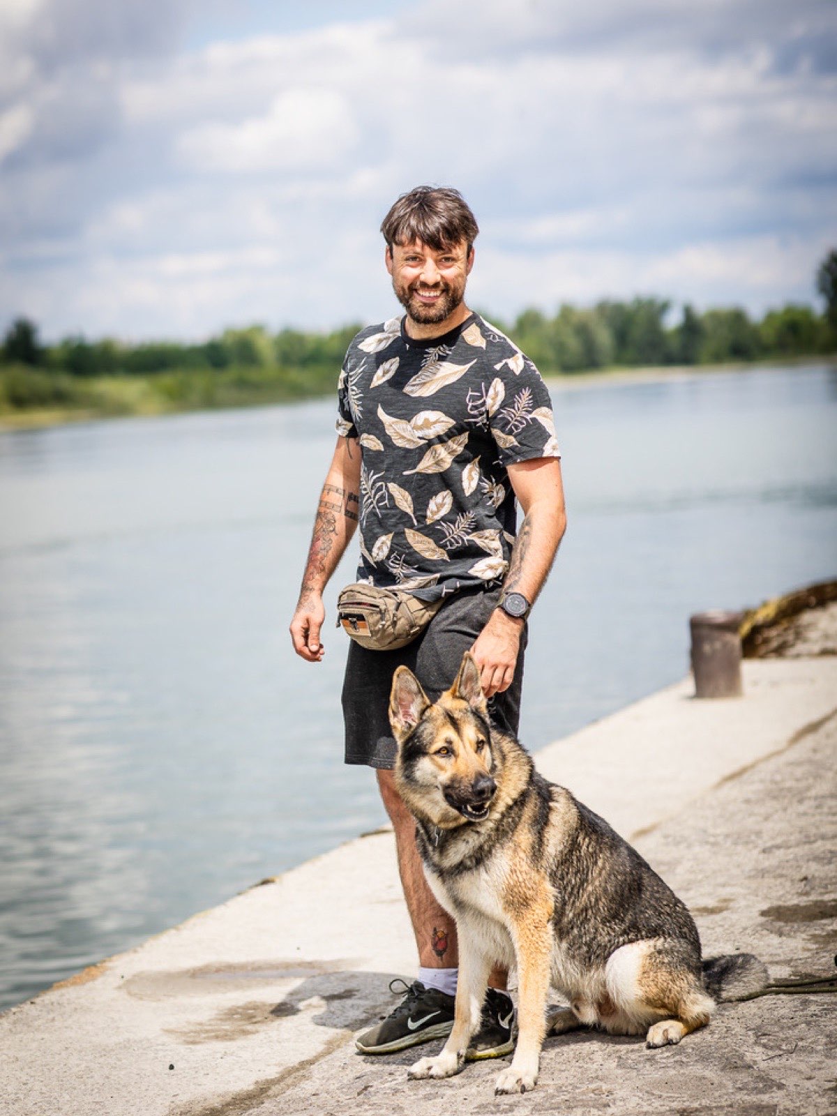 Michi steht am Wasser; Milo sitzt vor ihm.