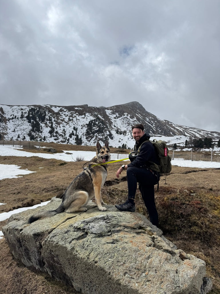 Michael Moser und Milo sitzen gemeinsam auf einem Felsen in den Bergen.